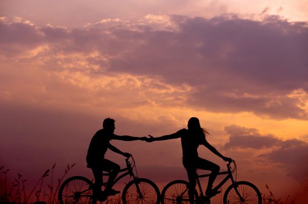 A couple on bikes holding hand in front of a sunset